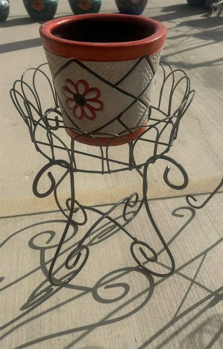 Wrought iron plant stand with a scrolled base holding a painted pot